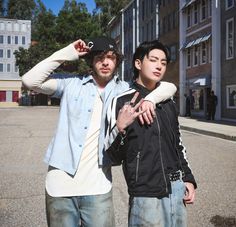 two young men standing next to each other on a street with buildings in the background