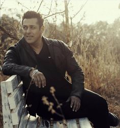 a man sitting on top of a wooden bench next to tall grass and dry trees