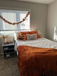 a bedroom decorated for halloween with pumpkins on the bed and garland hanging from the window