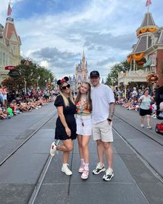 two women and a man are standing in front of a crowd at disney's castle