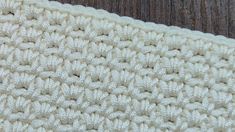 a close up view of a crocheted blanket on a wooden surface, with the bottom part showing