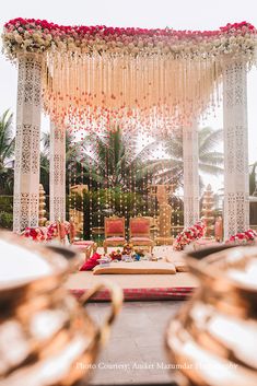 an outdoor wedding setup with gold plates and red flowers on the table in front of it