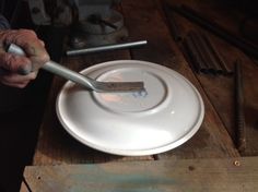 a person holding a fork over a white plate on top of a wooden table next to tools