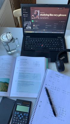 a laptop computer sitting on top of a desk next to a notebook and calculator