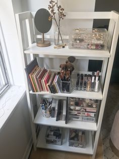 a white book shelf filled with lots of books and other items next to a window