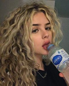 a close up of a person drinking from a water bottle with long curly blonde hair