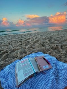 an open book sitting on top of a blue and white blanket next to the ocean