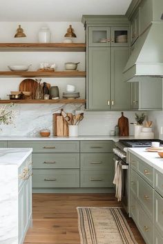 a kitchen with green cabinets and white counter tops, wooden flooring and open shelving