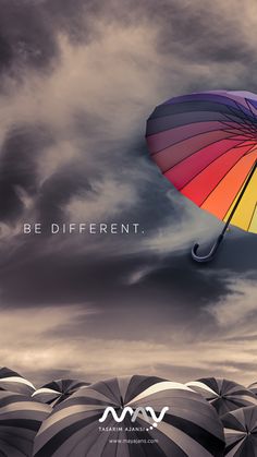 a colorful umbrella floating in the air above many black and white umbrellas under a cloudy sky