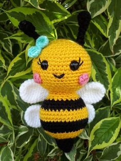 a crocheted bee with a blue bow on it's head sitting in some leaves