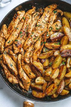 chicken and potatoes in a skillet on a white table with silver utensils