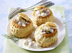 three biscuits covered in cream on a white plate next to a fork and napkin with silverware