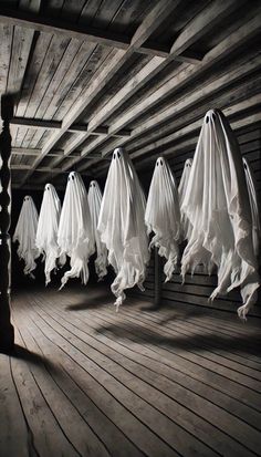 there are many white cloths hanging from the ceiling in an old room with wood flooring