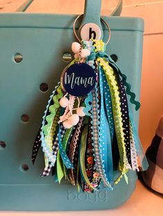 a blue purse with a name tag hanging from it's front loop and colorful ribbons attached to the handle