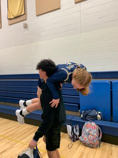 a man is holding a young boy on his back while he stands in the middle of a gym