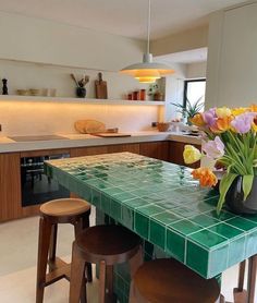 a green tiled table with stools and flowers in a vase on the counter top