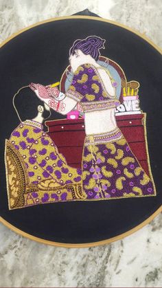 an embroidery work on a black cloth with a woman sitting in a chair