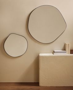 two circular mirrors mounted on the wall next to a white table with a stack of books