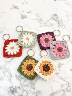 four crocheted keychains with flowers on them sitting on a marble surface