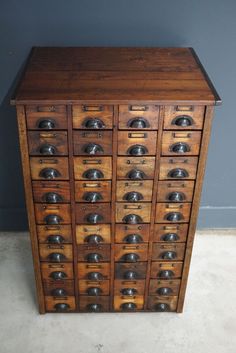 an old wooden cabinet with many drawers and bells on the top shelf, in front of a gray wall