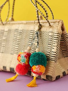 two colorful pom poms hanging from a woven purse