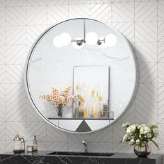 a bathroom vanity with a round mirror above it and flowers in vase on the counter