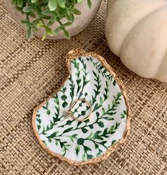 a white and green leaf shaped dish next to a potted plant with a wedding ring on it