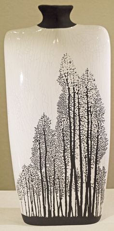 a black and white vase sitting on top of a table next to a wall with trees painted on it