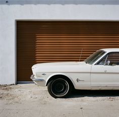 an old white car is parked in front of a garage door with shutters on it