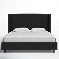 a bed with white pillows and black headboard on it's side, in front of a white wall