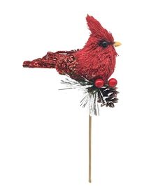 a red bird sitting on top of a wooden stick with pine cones and berries around it