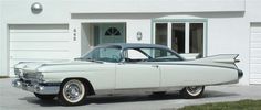 an old fashioned car parked in front of a white building with garage doors and windows