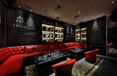 a room filled with lots of red couches next to a wall covered in wine bottles