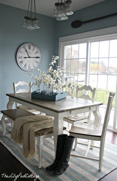 a dining room table with four chairs and a clock on the wall