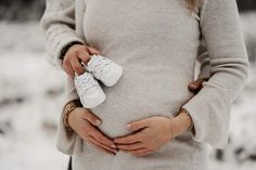 a pregnant woman is holding her shoes in the snow while she holds her belly with both hands