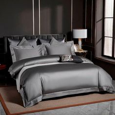 a large bed with blue sheets and pillows in a dark room next to a window