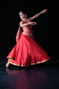 a woman in a red and gold dress is dancing with her arms out to the side