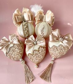 four ornaments with tassels and bows are on a pink surface, one has a heart