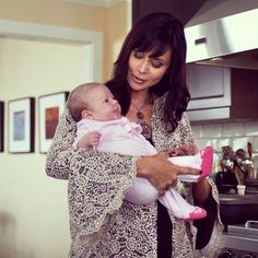 a woman holding a baby in her arms while standing next to a stove top oven