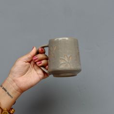 a hand holding a gray coffee mug in front of a grey wall