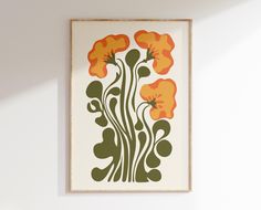 an orange and green floral print hangs on the wall next to a vase with flowers in it