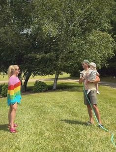 two women are standing in the grass while one holds a baby and another is holding a frisbee