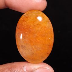 a person holding an orange stone in their left hand, on a black background that appears to be oval