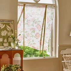 an open window in a living room with flowers on the curtains and blinds behind it