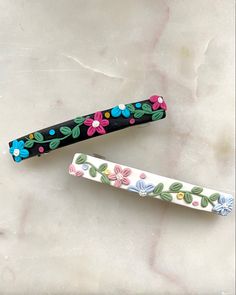 two pens with flowers painted on them sitting next to each other in front of a marble surface