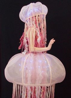 a mannequin dressed as a jellyfish with pink hair and white dress, standing in front of a black background