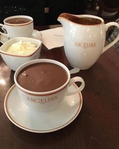 three cups of hot chocolate and two bowls of whipped cream on a table with an empty plate