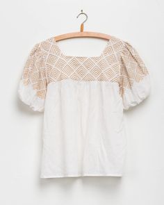 a white top with gold print on the chest and shoulders, hanging from a wooden hanger