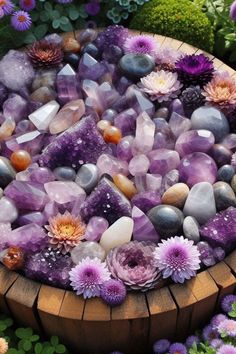 a wooden bowl filled with lots of purple rocks and flowers next to green plants on the ground