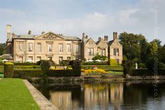 a large house sitting on top of a lush green field next to a lake in front of it